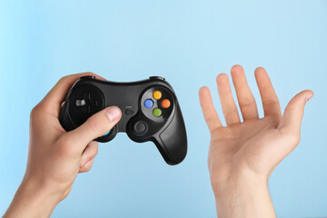 Fototapeta premium Man using wireless game controller on light blue background, closeup