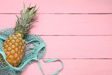 String bag with fresh pineapple on pink wooden background, top view. Space for text