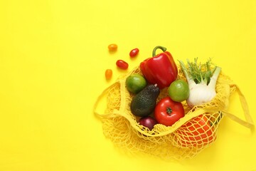 String bag with fresh vegetables and fruits on yellow background, flat lay. Space for text