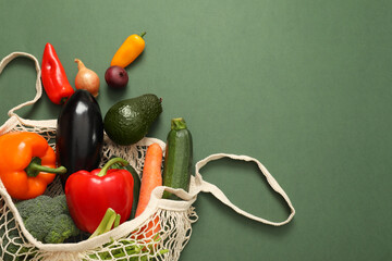 String bag with fresh vegetables on green background, flat lay. Space for text