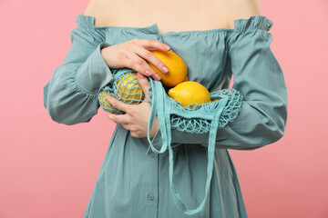 Woman with string bag of fresh lemons on pink background, closeup