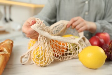 Woman with string bag of fresh fruits at light marble table, closeup