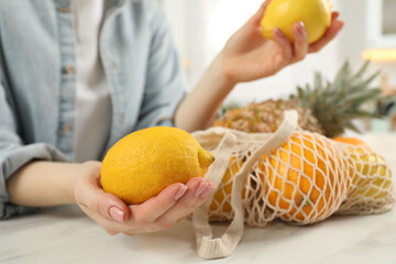 Woman with lemons and string bag of fresh fruits at light table, closeup