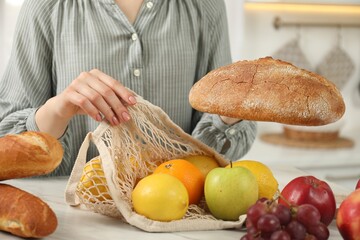 Woman with string bag of fresh fruits and bread at light marble table, closeup