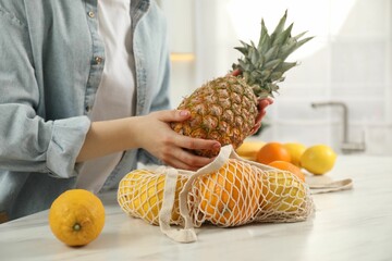 Naklejka premium Woman taking pineapple out from string bag at light marble table, closeup