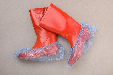 Rubber boots in shoe covers on grey background, top view