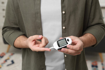 Diabetes test. Man checking blood sugar level with glucometer at home, closeup