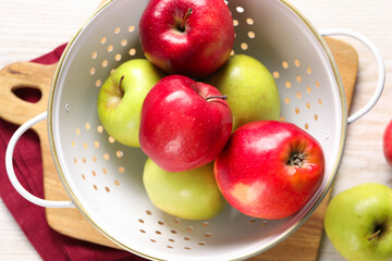 Fresh apples in colander on white wooden table, flat lay