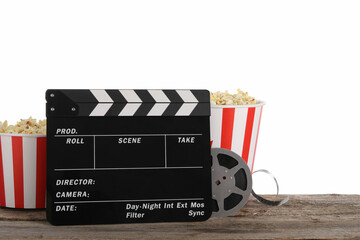 Movie clapper, buckets of tasty popcorn and film reel on wooden table against white background