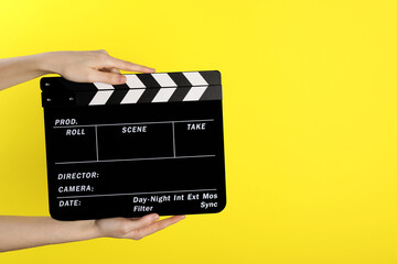 Woman holding movie clapper on yellow background, closeup. Space for text