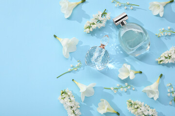 Luxury perfumes and floral decor on light blue background, flat lay. Space for text