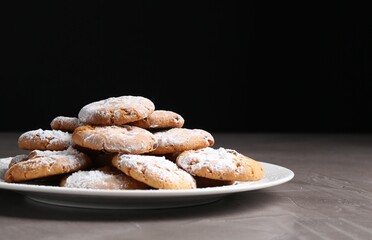 Woman with sieve sprinkling powdered sugar onto cookies at grey textured table, closeup