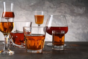 Different delicious liqueurs in glasses on grey table