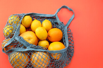 String bag with oranges and lemons on red background, top view