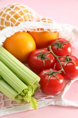 String bag with different vegetables and fruits on pink background, closeup
