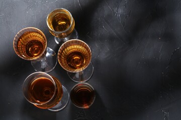 Many different liqueurs in glasses on dark textured table, flat lay. Space for text