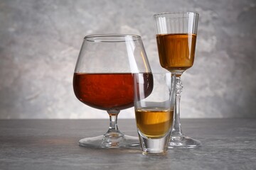 Different liqueurs in glasses on grey textured table, closeup