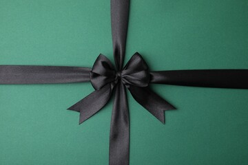 Black satin ribbon with bow on green background, top view