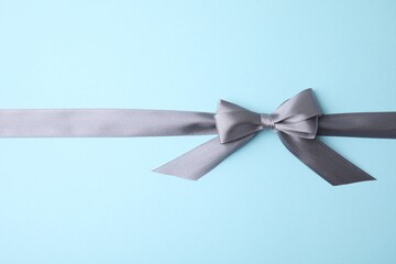 Grey satin ribbon with bow on light blue background, top view