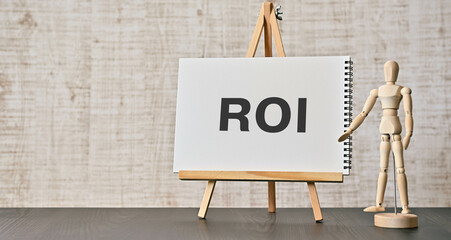 There is notebook with the word ROI. It is an abbreviation for Return On Investment as eye-catching...