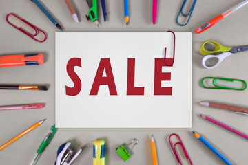 Sale text on sheet of office paper. Message in red on white page with paper clip. Top view or flat lay. Back to School Sales. Template for advertising, website, School supplies store