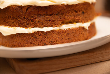 A slice of cake with a white frosting on a white plate. The cake is cut in half and placed on a wooden table