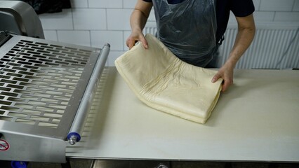 Raw puff pastry on a conveyor before freezing. Semi-finished products. The cook unwinds a huge...