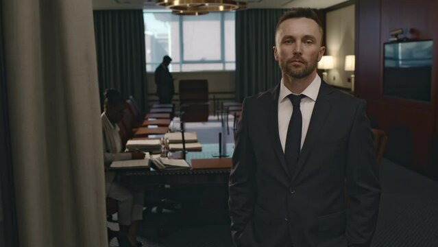 Medium portrait of confident male Caucasian legal firm CEO in expensive suit and tie posing in boardroom and looking at camera