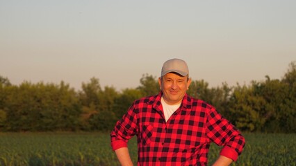 Naklejka na ściany i meble Portrait smiling man farmer posing at sunset sunny corn field countryside nature closeup. Male agronomist agricultural worker standing maize plantation organic harvest cultivation tree sky landscape