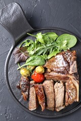 Delicious grilled beef meat, vegetables and greens on black table, top view