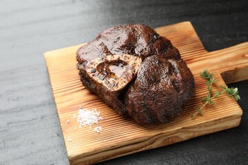 Piece of delicious grilled beef meat, thyme and salt on black table
