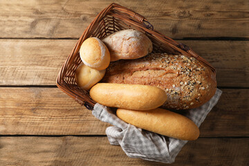 Wicker basket with different types of bread on wooden table, top view