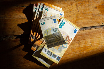 Euro bills arranged on a wooden table, illuminated by a beam of light.Income in European countries....