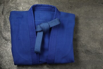 Blue karate belt and kimono on gray textured background, top view