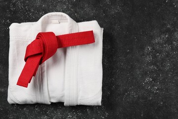 Red karate belt and white kimono on gray textured background, top view. Space for text