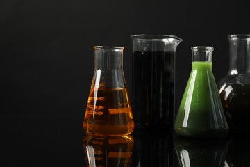 Glass flasks and beaker with different types of oil on black background