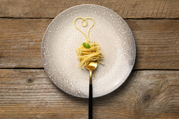 Heart made with spaghetti and fork on wooden table, top view