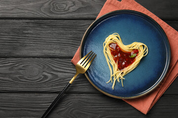 Heart made with spaghetti and sauce on black wooden table, top view. Space for text