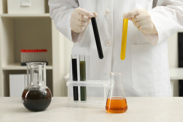 Laboratory worker holding test tubes with different types of crude oil at light marble table,...