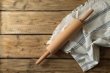 Rolling pin and kitchen towel on wooden table, top view. Space for text