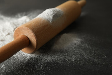 Scattered flour and rolling pin on black table, closeup