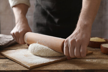 Man rolling raw dough at wooden table, closeup