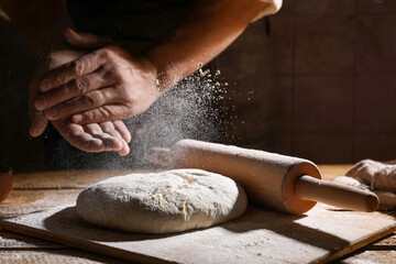 Man sprinkling flour over dough at wooden table, closeup