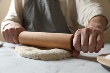 Man rolling raw dough at white table, closeup