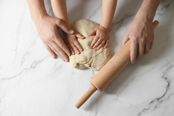 Father and child making dough at white table, top view