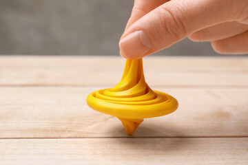 Woman playing with yellow spinning top at light wooden table, closeup