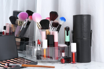 Bright lip glosses among different cosmetic products on white dressing table