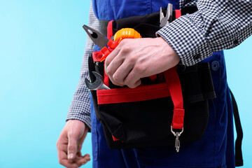 Young man with pliers and other tools in bag on light blue background, closeup
