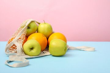 String bag with fresh apples and oranges on color background, space for text