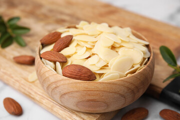 Fresh almond flakes and nuts in bowl on white table, closeup